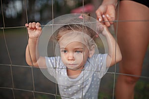 Toned portrait of Sad little girl looks through wire fence