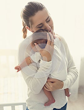 Toned portrait of smiling caring mother holding baby boy on hand