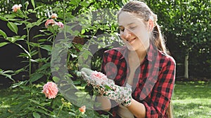 Toned portrait of smiling young woman holding growing pink rose in hand at backyard garden