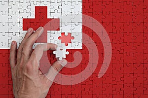 Tonga flag is depicted on a puzzle, which the man`s hand completes to fold