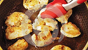 Tongs overturn fried chicken in a pan in oil