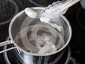 Tongs removes clean spoon from boiling solution