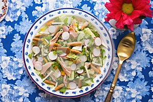 tongs serving fattoush onto a plate, blue tablecloth