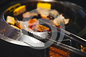 Tongs wait for grilling beef with food on charcoal stove background