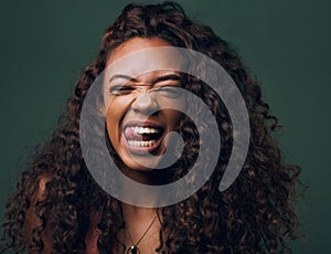 Tongue out, portrait and young woman in studio with natural curly hair, happy meme or wink on a green background. Face
