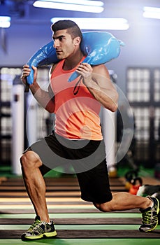 Toning every inch. a young man working out with a sandbag at the gym.