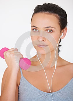 Toning up for Summer. Portrait of a young woman working out with weights while listening to music.