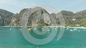 Tonsai Bay unspoilt exotic paradise harbouring fleet of small boats in Ko Phi Phi Don Island, Thailand - Aerial Fly-over shot