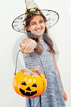 Too cute to be spooky. a little girl wearing a witch hat while holding a jack o lantern against a white background.