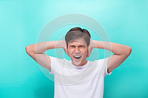 Too loud. Frustrated young man covering ears with hands and looking at camera while standing grey background