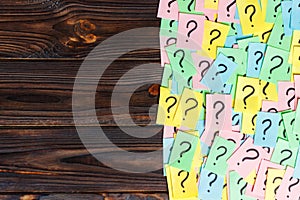 Too Many Questions on wooden background. Pile of colorful paper notes with question marks. top view copy space