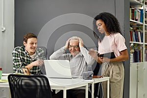 Too much information, Aged man senior intern touching head with hands while listening to his young colleagues, Friendly