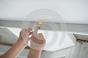 Tool level in men's hands and a flat horizontal surface of the ceiling. Styrofoam, seiling mounting.