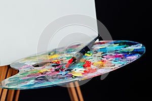 Tools of the artist. Brushes, wooden easel tripod, palette colorful. Black background, studio, nobody.