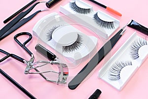 Tools for eye lash extension on pink background. Fake eyelashes, tweezers, brush and eyelash curler. Makeup cosmetics.