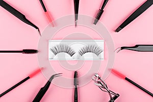 Tools for eye lash extensions on pink background. Eyelash curler, tweezers, brushes. Makeup accessories. Fake eyelashes.