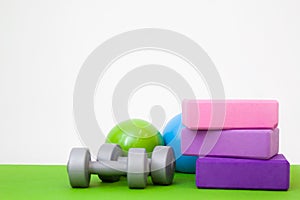 Tools for fitness exercises - pink and purple blocks, balls and dumbbell on green mat. free space for text - gymnastic, stretching