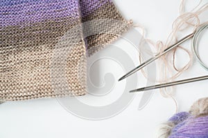 Tools for needlework: knitting fabric, tangle of thread of multicolored yarn, knitting needles. Purple, brown, white, beige colors