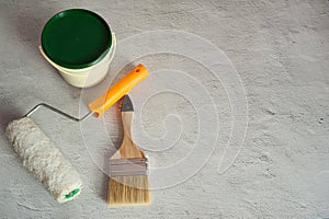 Tools for painting, brush, paint roller and a can of paint on a concrete background.