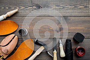 Tools for shoe repair. Hummer, awl, knife, sciccors, wooden shoe, insole, paint and leather. Dark wooden background top