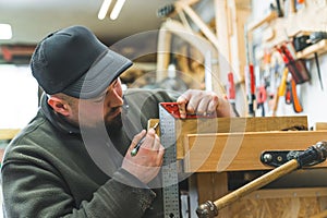 Tools in woodworking process. Focused craftsman using bracket and marking on wood with a pencil. Carpenter workshop