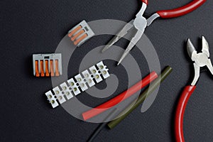 Tools for working with electricity, terminal blocks and heat shrink tubes lie on a dark background