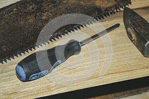 Tools for working with wood. On a wooden background lies a hammer, a saw and a screwdriver