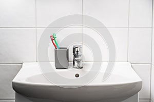 Toot brush cup in bathroom and toilet sink. Toothbrush in clean restroom. Water tap, faucet and basin to wash hands in WC.