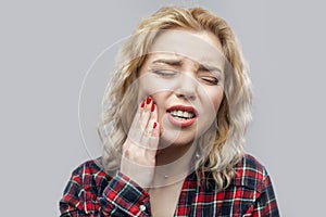 Tooth ache. Portrait of beautiful blonde young woman in casual red checkered shirt standing and touching her painful teeth with