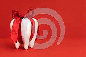 Tooth as a gift. A large white modal molar is tied with a red ribbon with a bow. Bright red background