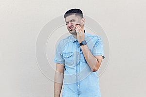 Tooth pain. Portrait of worry sad handsome young bearded man in blue shirt standing, touching his cheek because feeling toothache