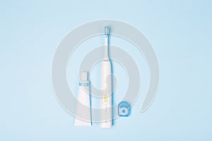 Tooth paste in tube, floss and tooth brush on light blue background. Copy space.
