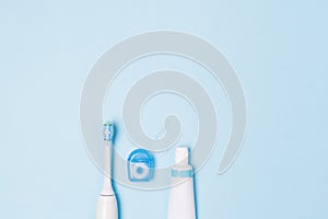 Tooth paste in tube, floss and tooth brush on light blue background. Copy space.