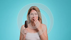 Tooth sensitivity. Middle aged woman biting ice-cream and suffering from acute toothpain, touching her painful jaw