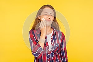 Toothache. Portrait of unhealthy girl in checkered shirt touching sore cheek, grimacing from sudden pain having dental problems