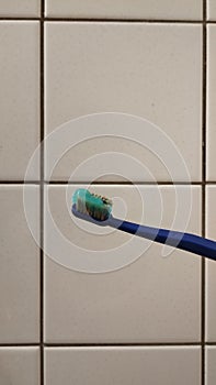a toothbrush with blue toothpaste on a white tile background