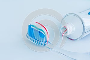 Toothbrush of clear plastic with blue bristles, white blue red toothpaste squeezes out of a tube