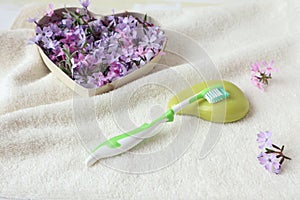 Toothbrush with fragrant soap on a white bath towel with a heart filled with delicate flowers, side view - a concept of pleasant