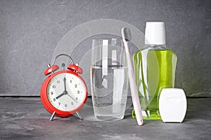 Dental and morning concept. Toothbrush, mouthwash, dental floss, glass of water and alarm clock on a gray background