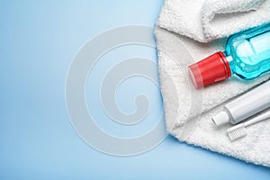 Toothbrush with paste tube, terry towel and mouthwash bottle on blue background. Top view, copy space