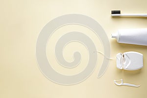 Toothbrush, toothpaste and dental floss on a yellow background with space for text, flat lay photo