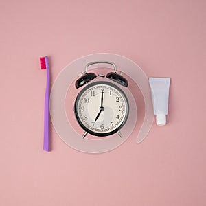 Toothbrush, tube of toothpaste and alarm clock on a pink background. Time to brush your teeth.