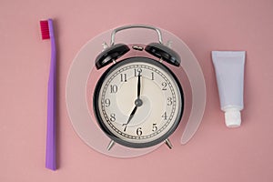 Toothbrush, tube of toothpaste and alarm clock on a pink background. Time to brush your teeth.