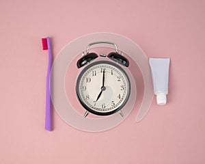 Toothbrush, tube of toothpaste and alarm clock on a pink background. Time to brush your teeth.