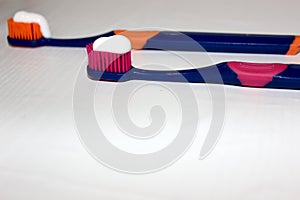 2 toothbrushes on a white background with toothpaste. Toothpaste on a toothbrush isolated on white. Pink toothbrush. Orange toothb