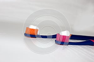 2 toothbrushes on a white background with toothpaste. Toothpaste on a toothbrush isolated on white. Pink toothbrush. Orange toothb