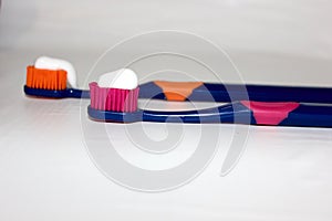 2 toothbrushes on a white background with toothpaste. Toothpaste on a toothbrush isolated on white. Pink toothbrush. Orange toothb