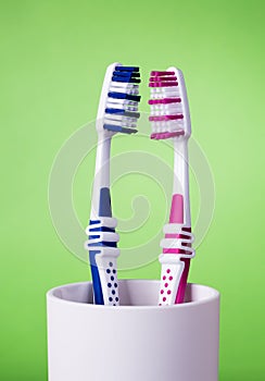 Toothbrushes in white cup on green background