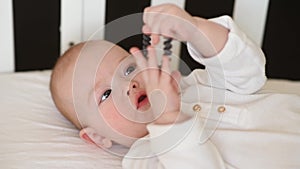 Toothless baby lies in a crib and nibbles an elastic band for hair. Teething in an infant