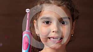 Toothless girl with an electric brush. The baby shows a toothless smile and an electric brush. Close up